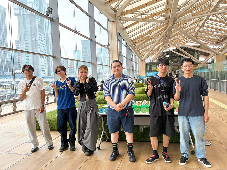 高輪ゲートウェイ駅の大きな膜屋根の下に並ぶ敬愛大学国際学部2年庄司ゼミの学生6人。SDGs目標3「すべての人に健康と福祉を」、6「安全な水とトイレを世界中に」、7「エネルギーをみんなに そしてクリーンに」、13「気候変動に具体的な対策を」、15「陸の豊かさも守ろう」の視点から、街の技術、環境、人への配慮を現地調査した。