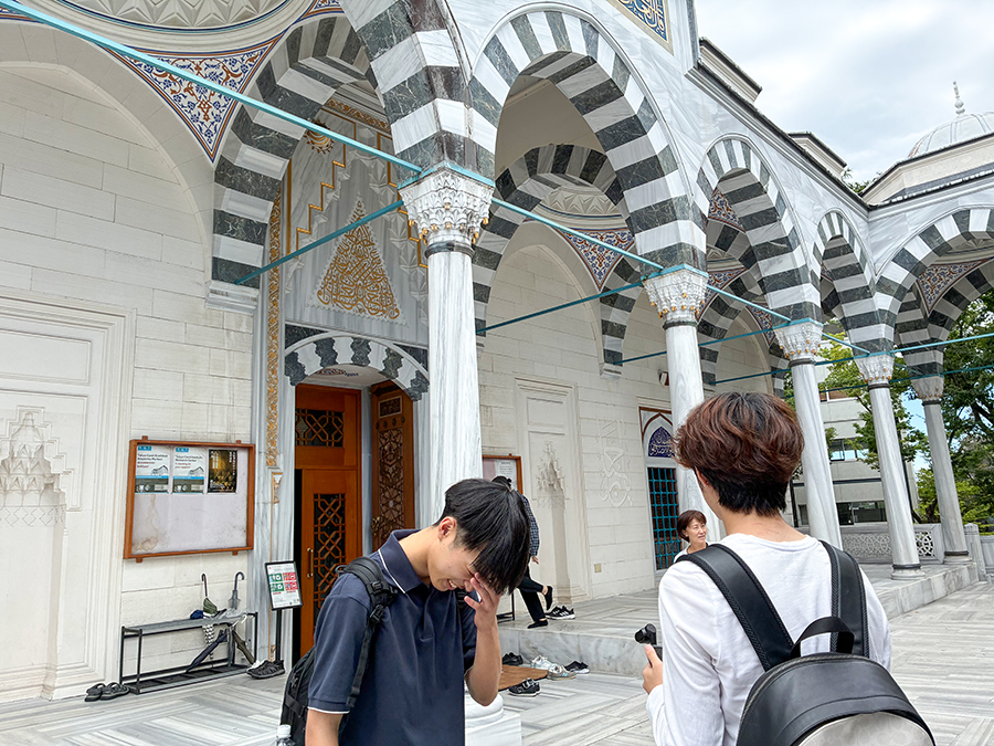 東京ジャーミイの幾何学模様で飾られたアーチと柱を見学する敬愛大学国際学部1年庄司ゼミの学生。礼拝堂の入口で靴を脱ぐ習慣を含め、イスラム建築と生活文化に触れている。